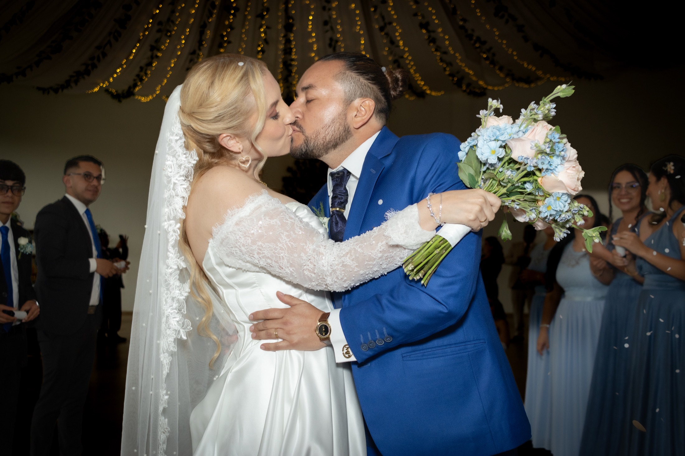 Novios besándose durante la recepción rodeados de invitados
