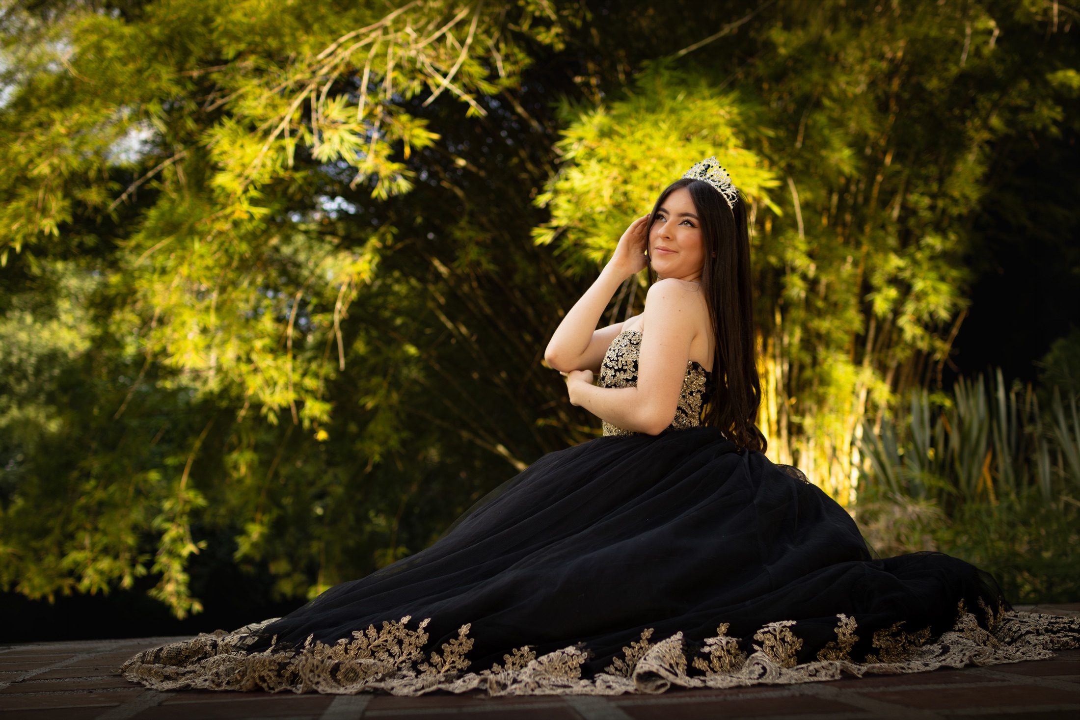Quinceañera con vestido negro y dorado en un jardín de bambú
