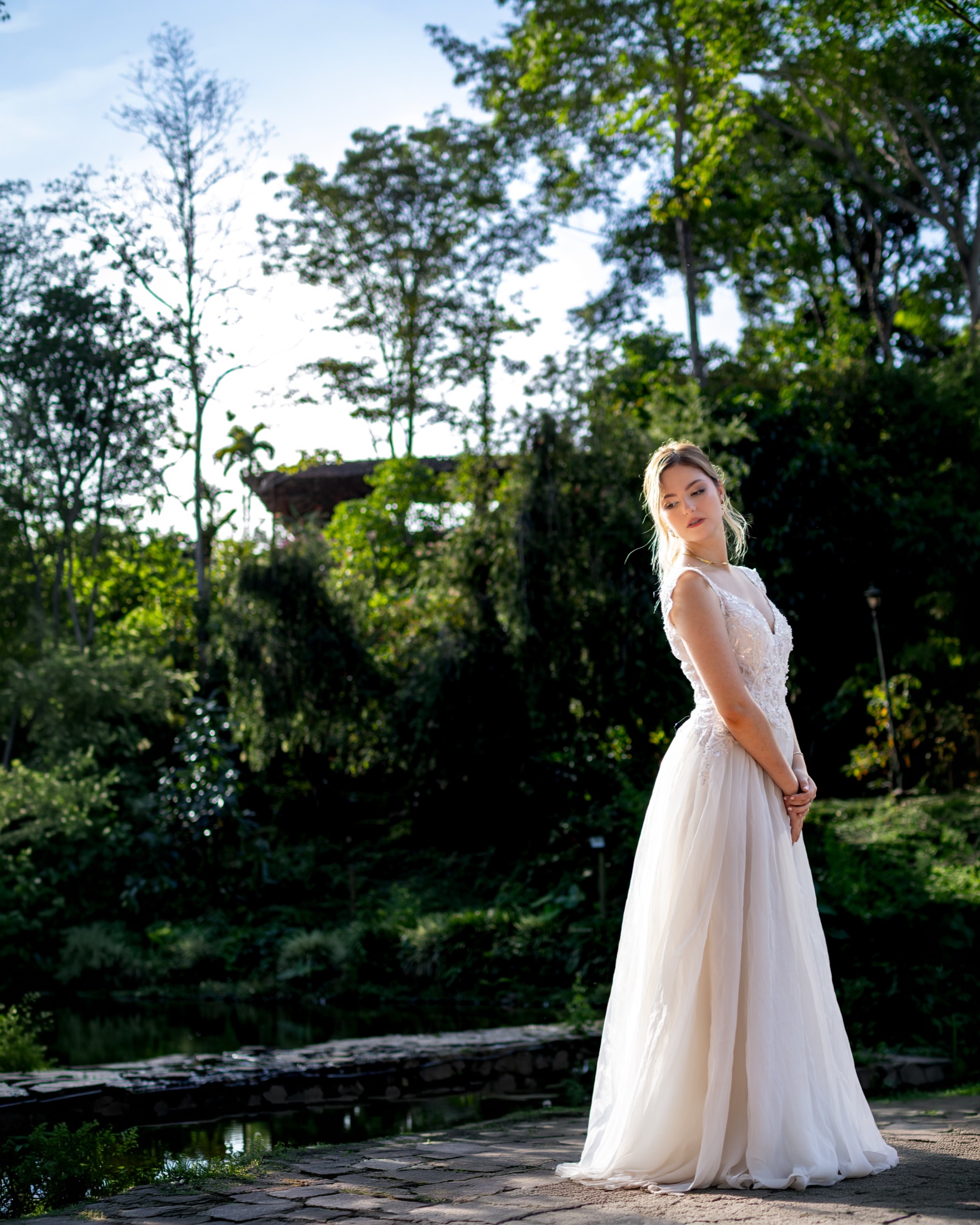 Novia de perfil junto a un lago rodeado de vegetación, mirando hacia abajo