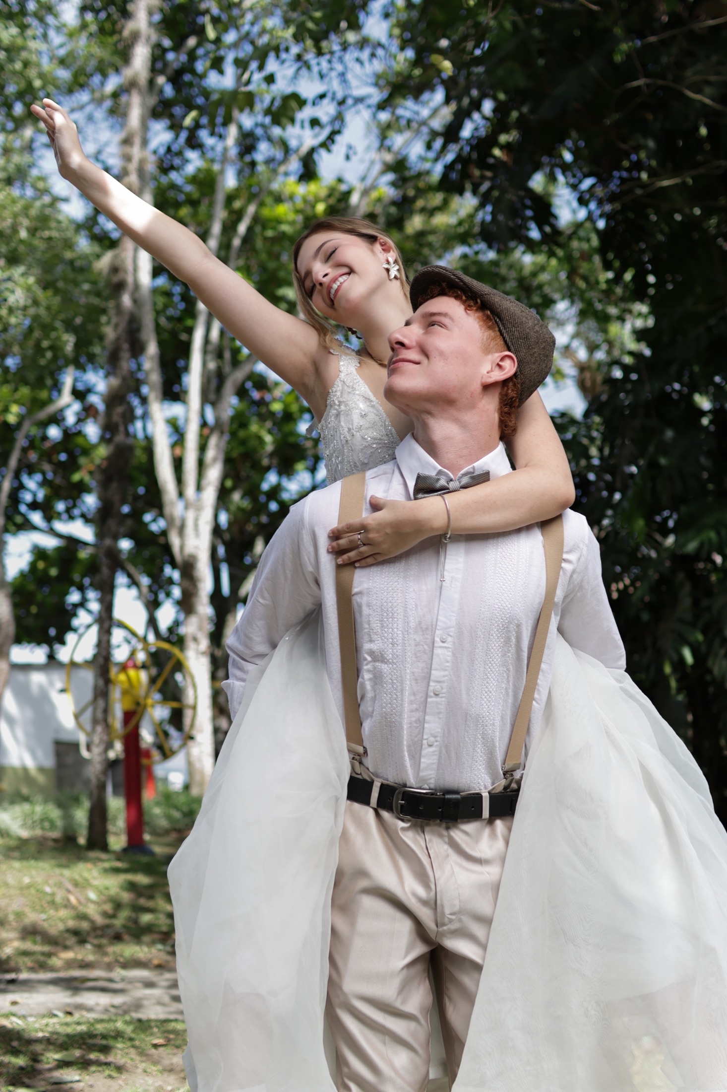Novia con el brazo extendido al cielo mientras su pareja la carga sonriendo