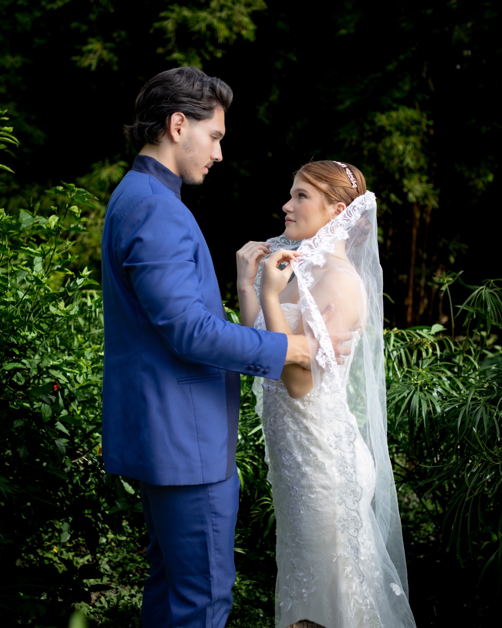 Novio ajustando el velo de la novia mientras se miran en un jardín