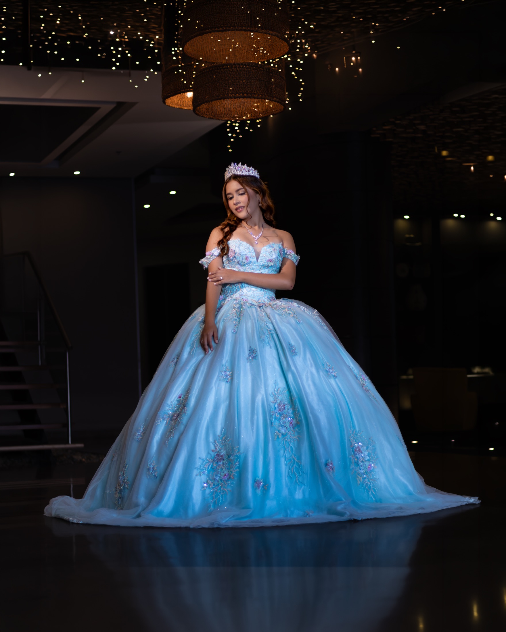 Quinceañera con vestido azul claro bajo una lámpara de fibra natural