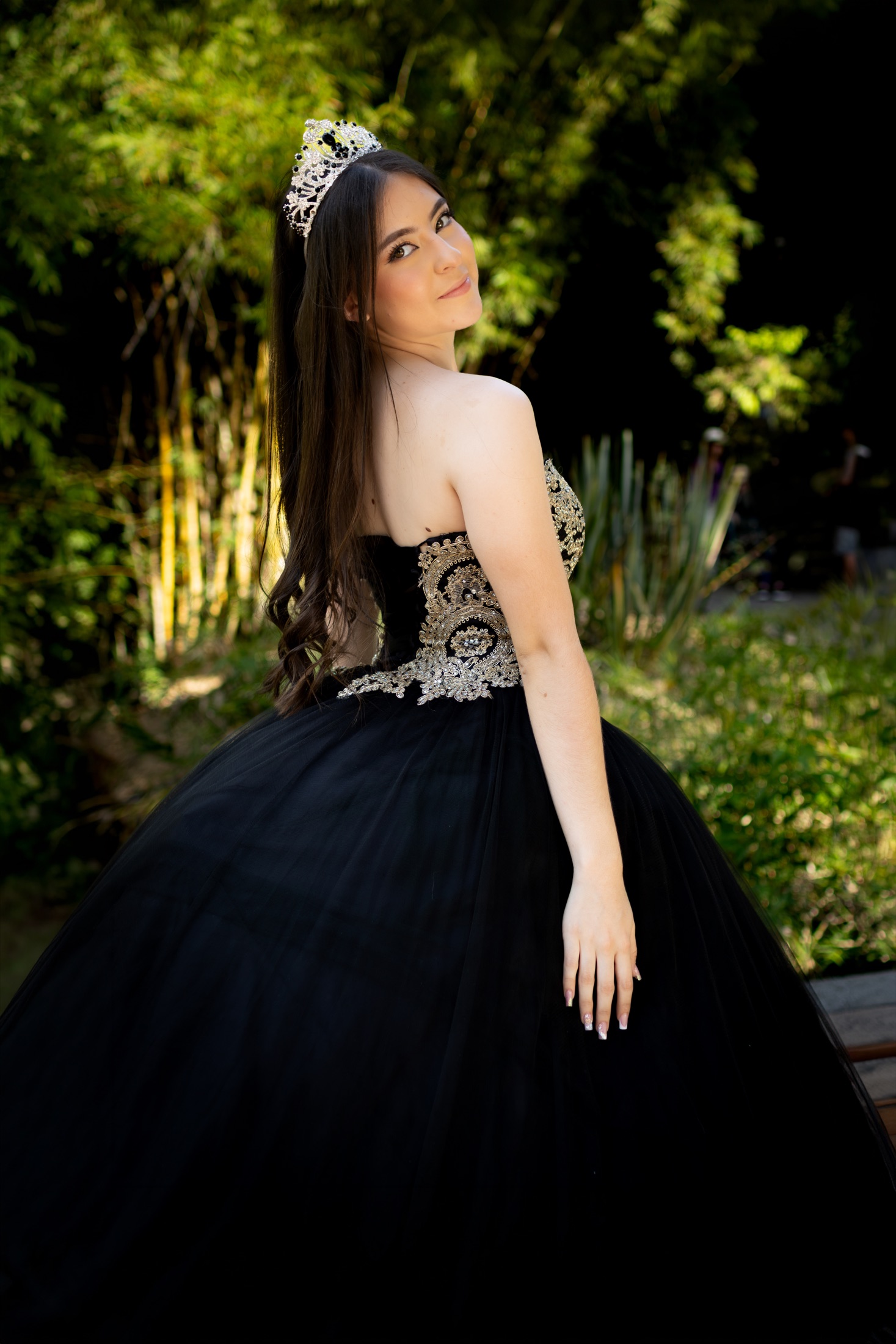 Quinceañera con vestido negro y dorado mirando por encima del hombro