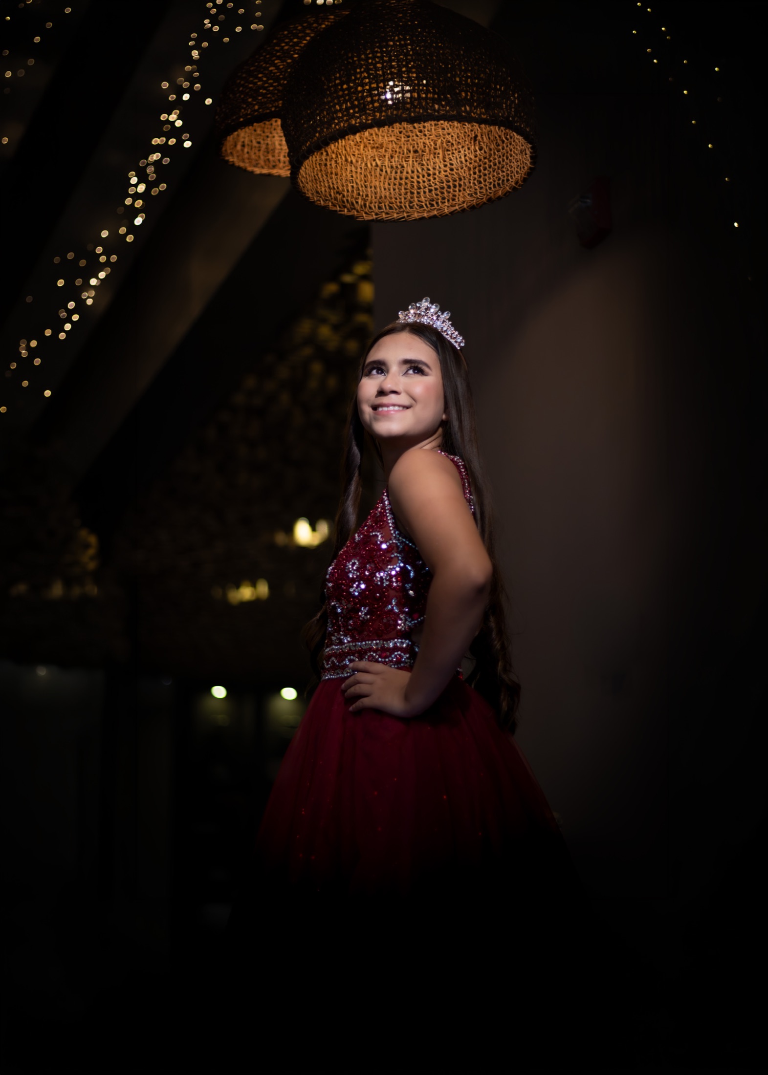 Quinceañera con vestido rojo bajo una lámpara y luces colgantes